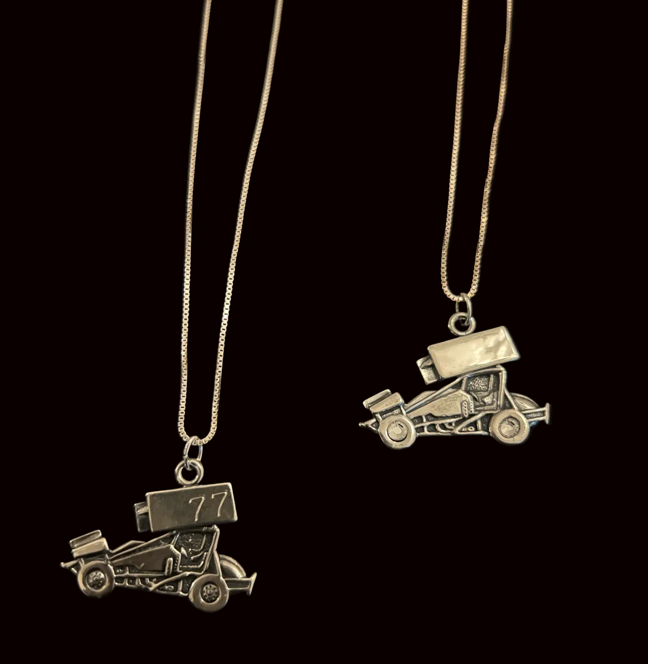 Two silver car-shaped pendants on chains against a black background