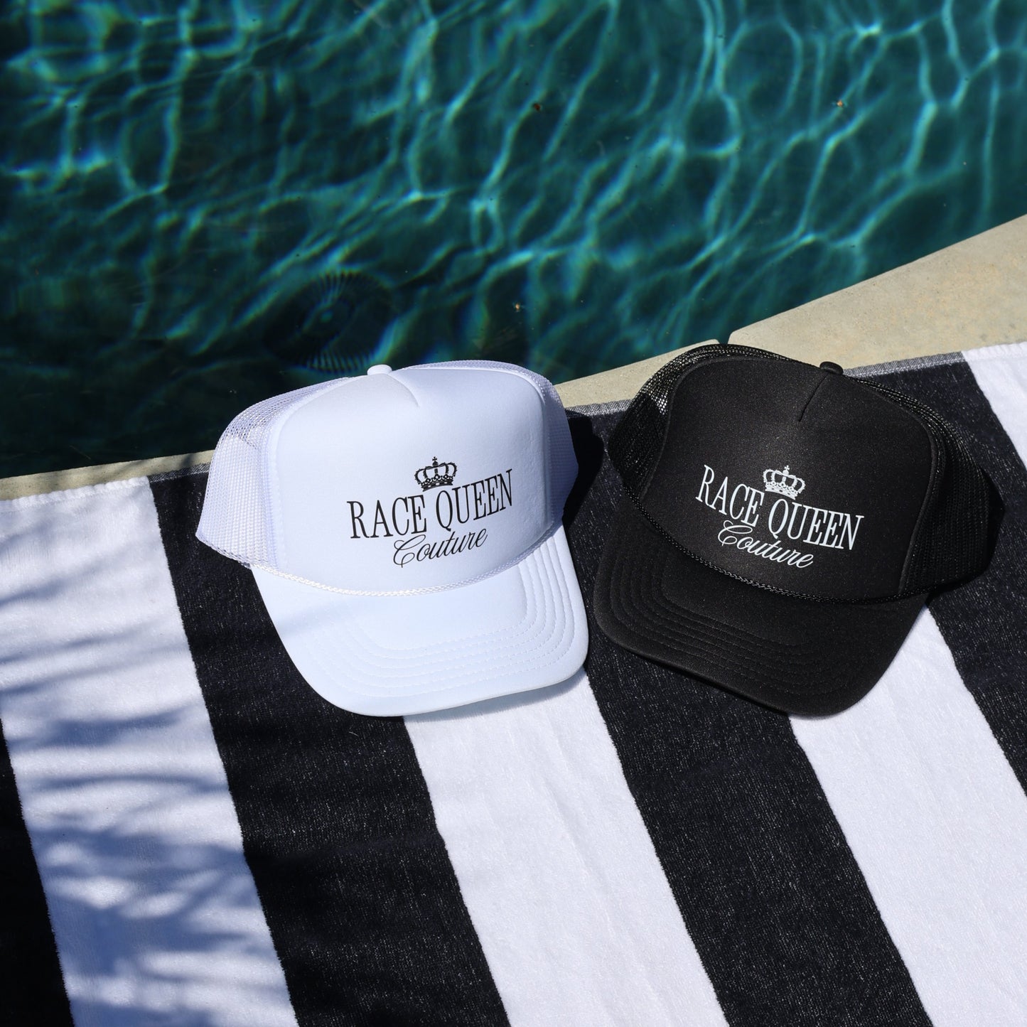 Two hats on a black and white striped towel by a pool